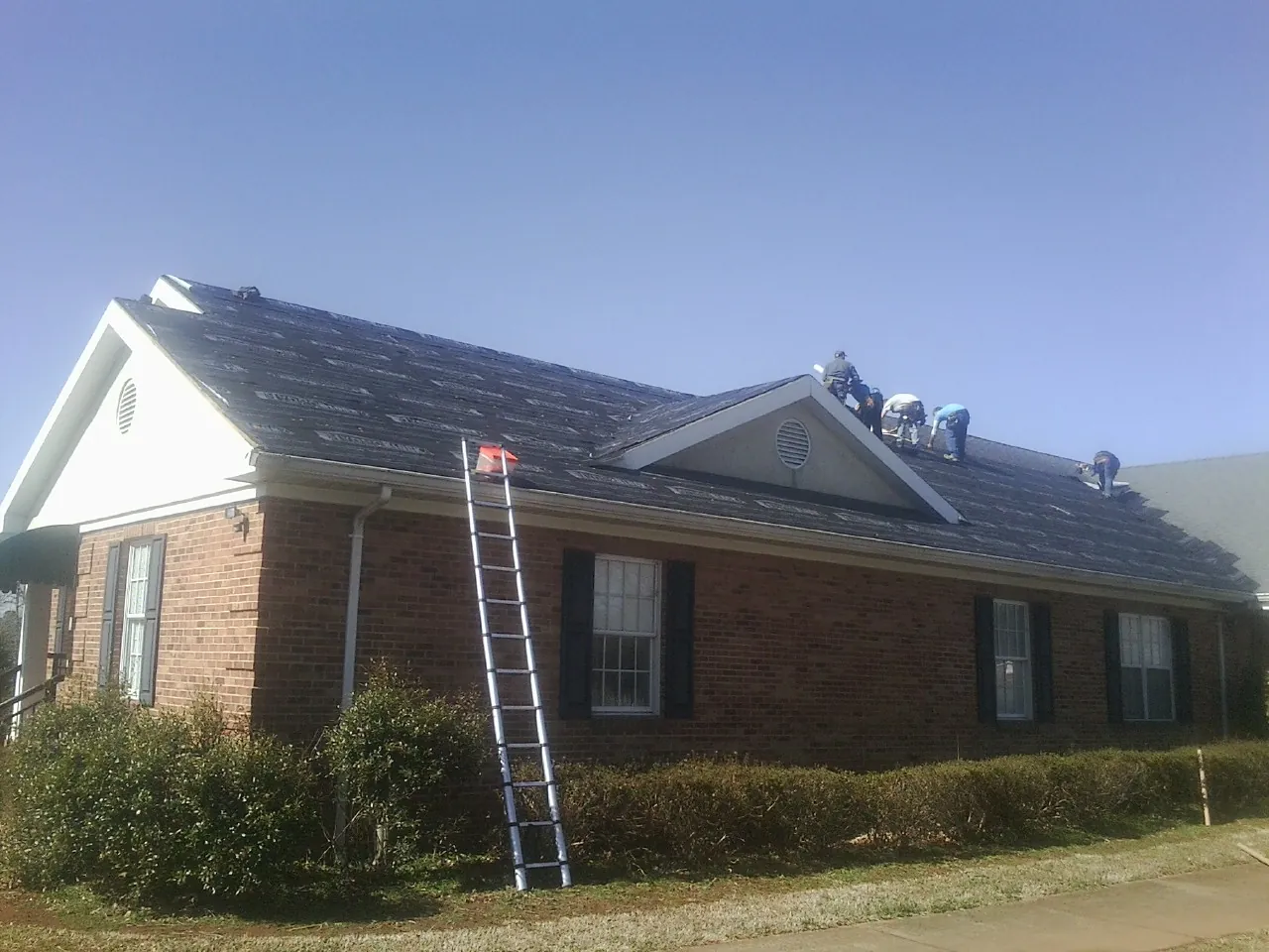 Crew tearing shingles off a brick ranch roof with a ladder set — Emergency Roof Repair work by our crew in Pilot Rock