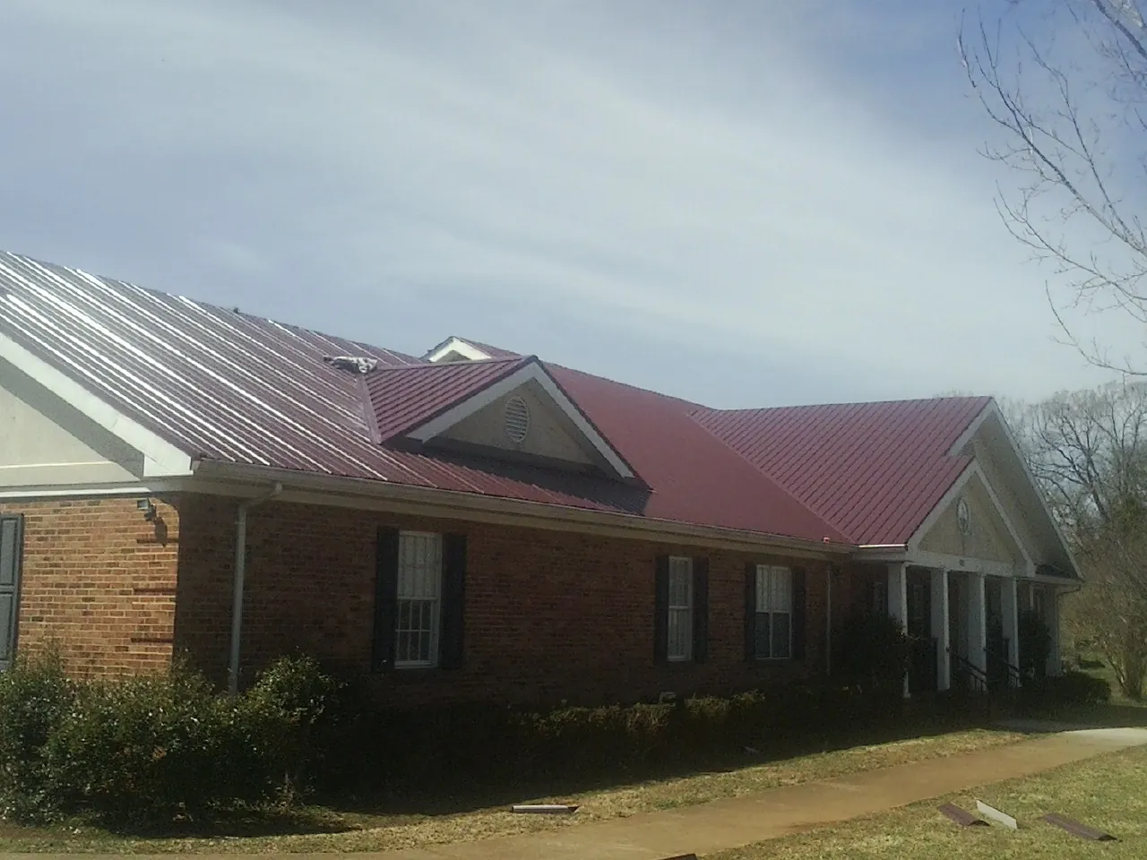 Red metal roof with gabled entries on a long brick building, from a Hail Damage Roof Repair job in Pilot Rock
