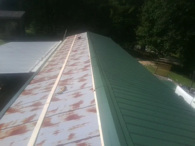 Old rusted panels beside newly installed green metal roofing — Wind Damage Roof Repair by Roofing Brothers in Pilot Rock