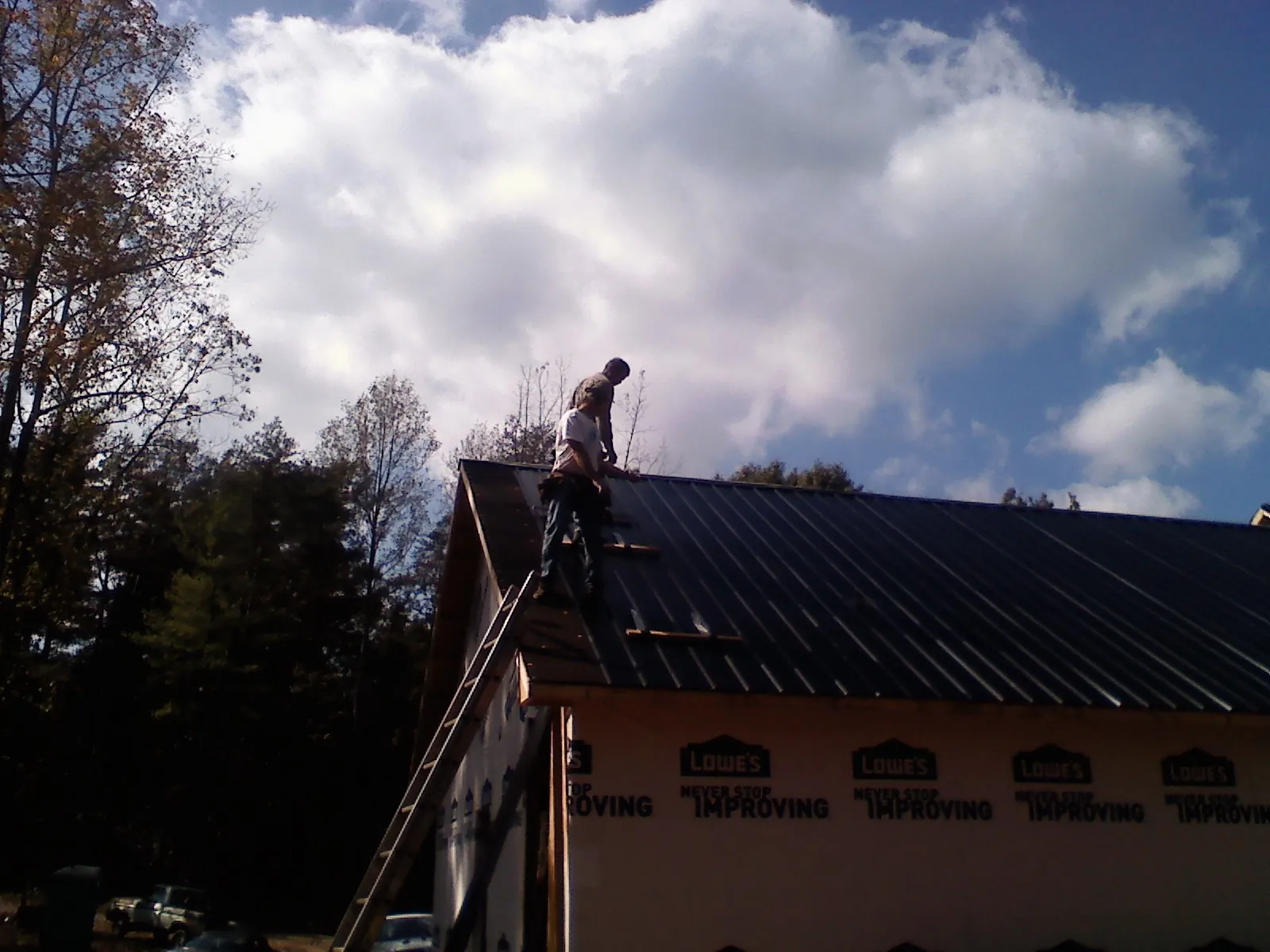 Roofer fastening dark metal panels high against a cloudy sky, from a Roof Inspection job in Pilot Rock