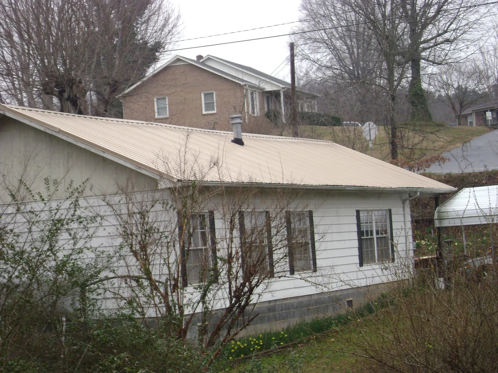 Tan metal roof on a white sided house set into a hillside — Commercial Roofing by Roofing Brothers in Pilot Rock